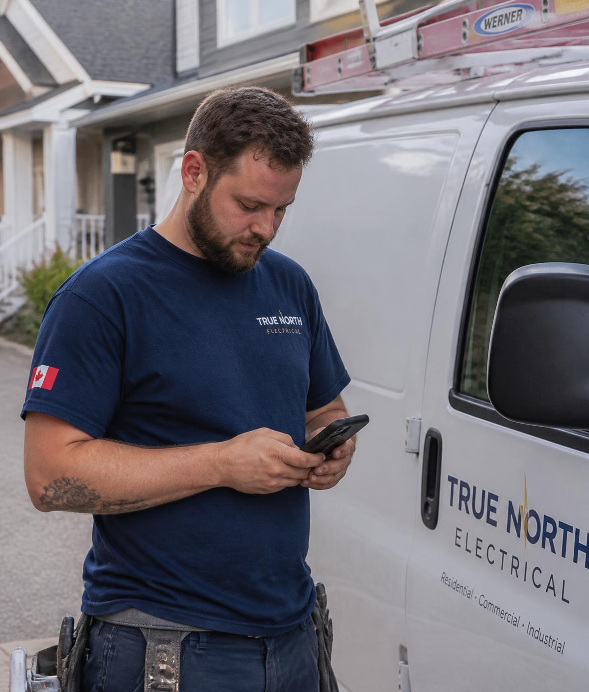 Electrician checking JobWorks365 on his phone beside his service van at a residential job